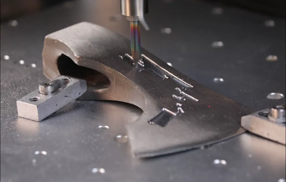Gweike C1 engraving a steel axe head held in fixture clamps